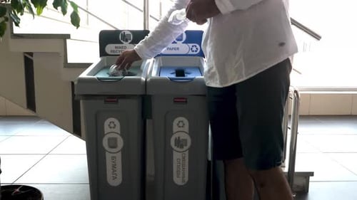A man throwing plastic container in a public recycle bin