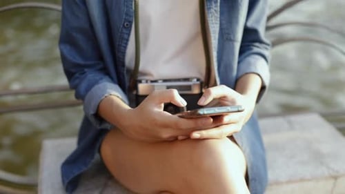 Asian woman using smartphone devices sharing social media while sitting beside Chao Phraya River.