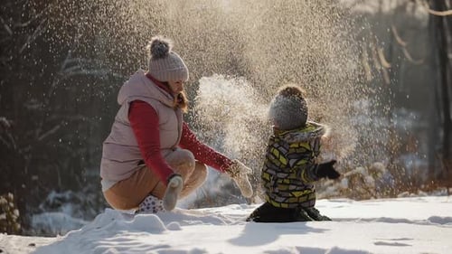 Glückliche Mutter mit kleinem Sohn spielt mit Schnee und wirft es hoch