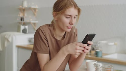 Woman Using Phone at Kitchen Table With Breakfast