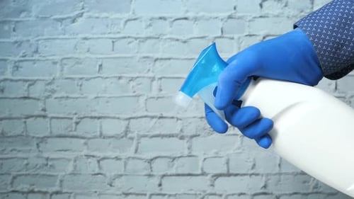 Hand with Glove Holds Cleaning Spray Bottle