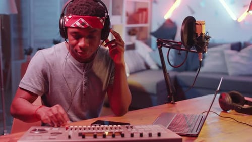 Young Black Musician Using Mixing Console and Laptop in Home Studio