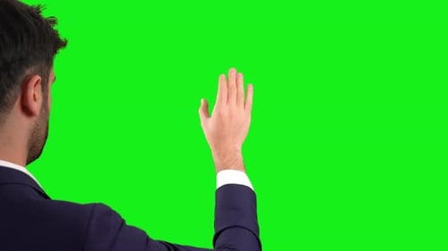 Businessman doing something with hands on digital screen. Green background.