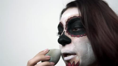 Woman Applies White Paint To Her Face with Sponge for Santa Muerte Makeup