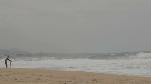 Surfer on Beach with City on Overcast Day
