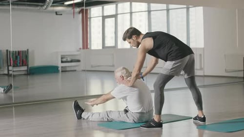 Pensioner Man Doing Stretching Exercise with Fitness Instructor in Gym Together
