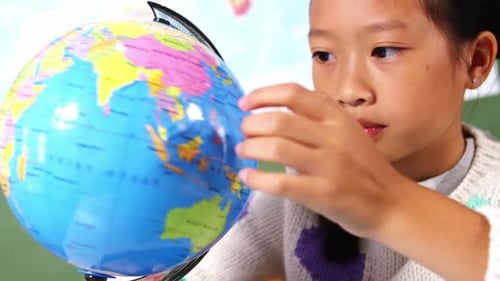 Schoolgirl looking at globe in classroom at school