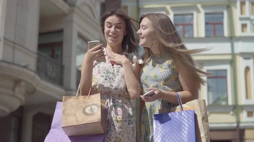 Young Women Looking at Phone With Shopping Bags