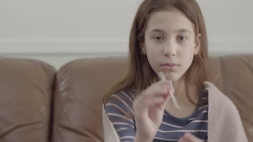 Portrait Tired Sick Girl Sit in Sofa, Looking at Thermometer and Showing It in the Camera