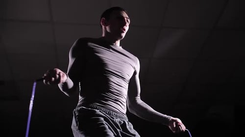 Man Exercising with Jump Rope in Dark Gym