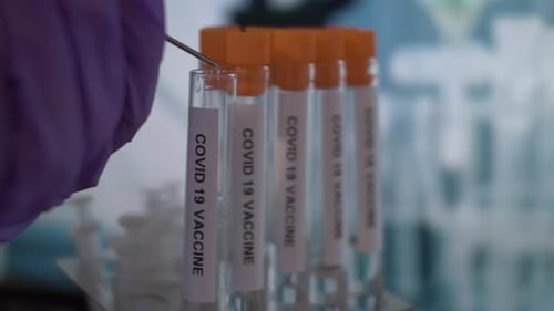 Tip Of Syringe Dripping Coronavirus Covid 19 Vaccine Into Test Tube Vial. Close Up, Locked Off