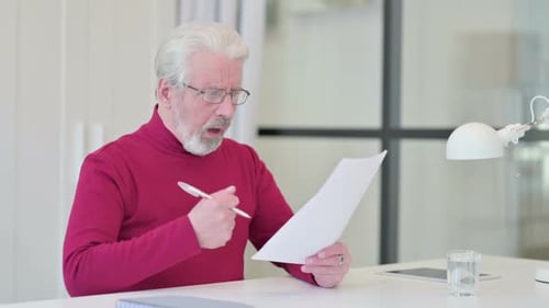 Senior Man Reviewing Documents at White Desk