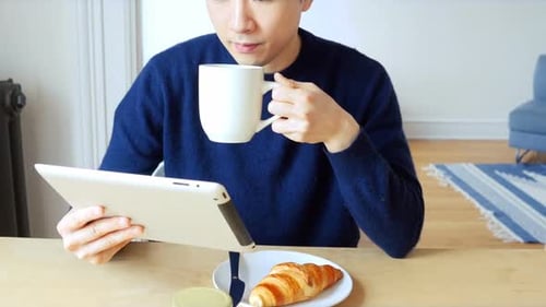 Young Adult Drinking Coffee and Using Tablet Indoors