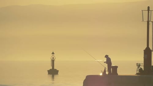 Um pescador em um cais ao pôr do sol