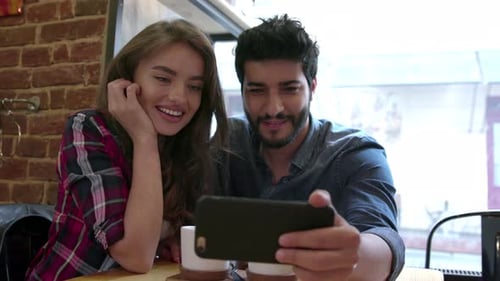 Video calling. Happy couple using phone for video call in cafe