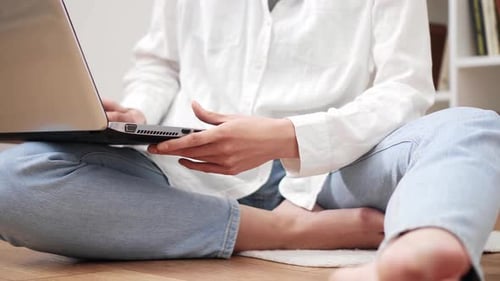 Un étudiant est assis par terre en train de taper un message sur un ordinateur portable. La fille Uchikni exécute la tâche