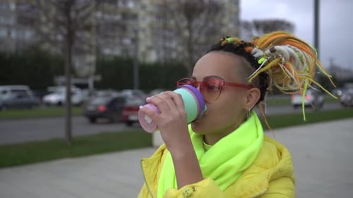 Woman Drinks Coffee on the Background of a City Street