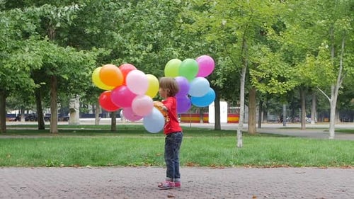 Child Holding Colorful Balloons Walking Through Park