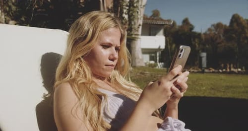 Blond Woman Texting On Smartphone In Sunny Garden