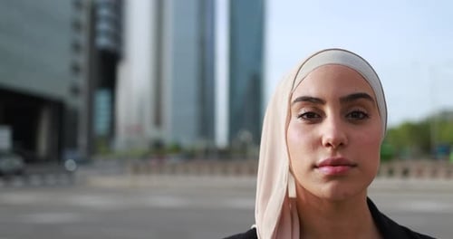 Muslimische Geschäftsfrau blickt in die Kamera im Freien mit Stadt im Hintergrund