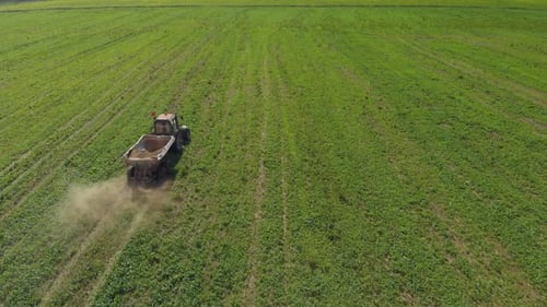 Tractor Spreads Fertilizer Across Green Farmland Aerial View