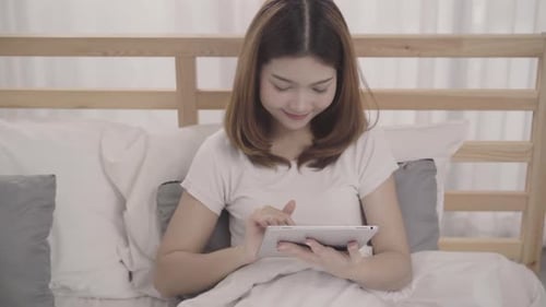 Woman Using Tablet in Bed Smiling