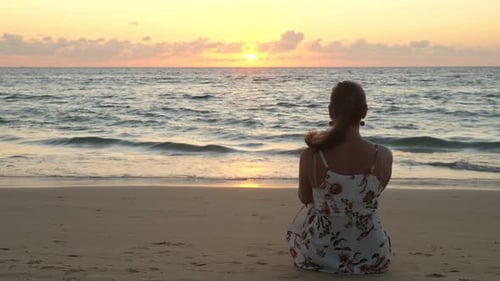 Young Woman in Stylish Dress Sits on Beach at Sunset Time