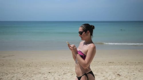 Young Woman in a Swimsuit with a Phone on the Beach