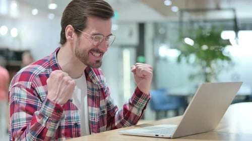 Young Man Cheering at Laptop in Modern Office