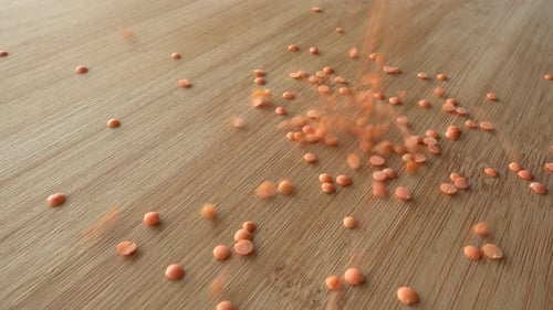 Red Lentils Being Poured Onto a Wood Surface