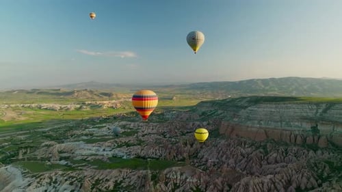 Hot air balloons fly over the mountainous landscape of Cappadocia, Turkey.