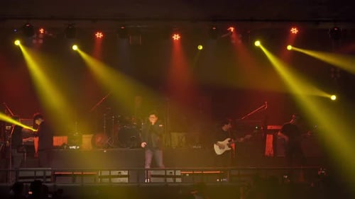A singer with music band performing on a stage concert with lighting laser beam spotlight show