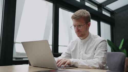 Adult Man with Glasses is Working with Laptop in Office or Coworking Typing Message or Report