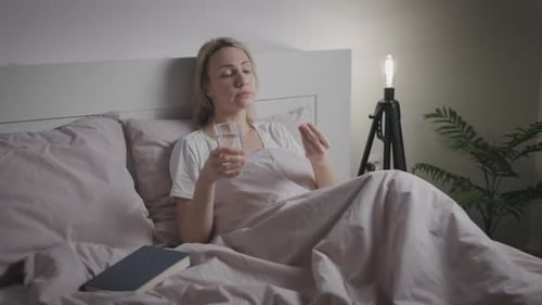 Woman Lying in Bed Taking Medicine