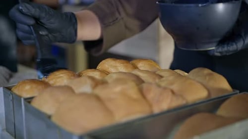 Gebäck, Bäcker mit Handschuhen schmiert frische heiße, duftende Brötchen aus frischem Weizenmehl mit Schnabel