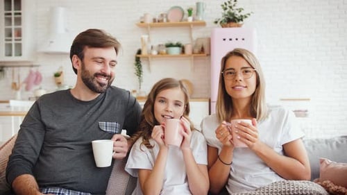 Smiling Family Relaxing on Sofa with Hot Drinks