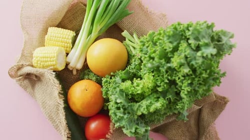 Vídeo de frutas y verduras frescas en bolsa rústica sobre fondo rosa