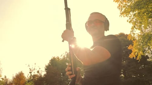 Man Stands with Rifle Outdoors in Sunlight
