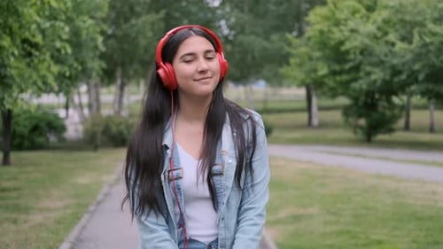 Stylish Cheerful Girl Dancing in the Park Listening To Music on Headphones