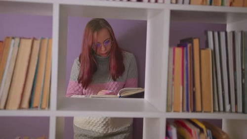 A Student is Reading a Book in the Library Behind the Bookshelves