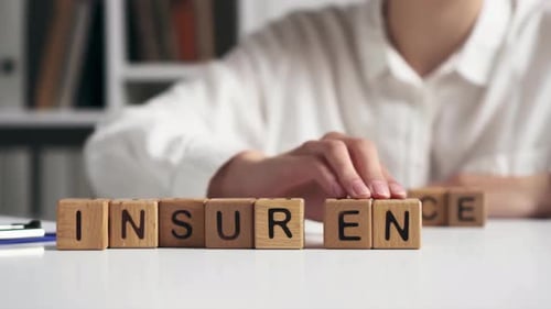 Hand Spells "Insurance" with Blocks on White Table