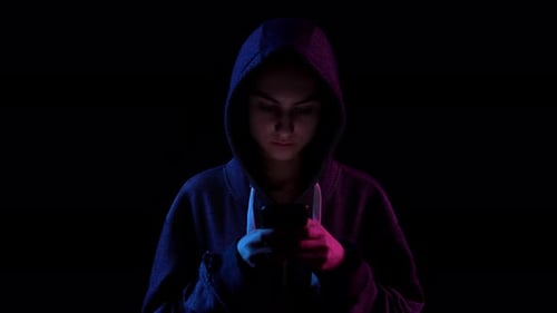 A Young Woman in a Hood with a Phone in Her Hands. Hacker Makes a Hack Through the Phone. Blue and
