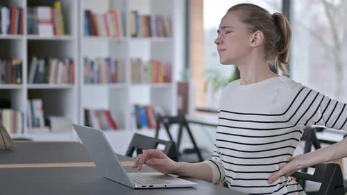 Young Woman with Back Pain Using Laptop in Library