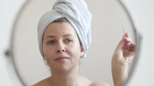 Woman Tweezing Eyebrows in Front of Mirror