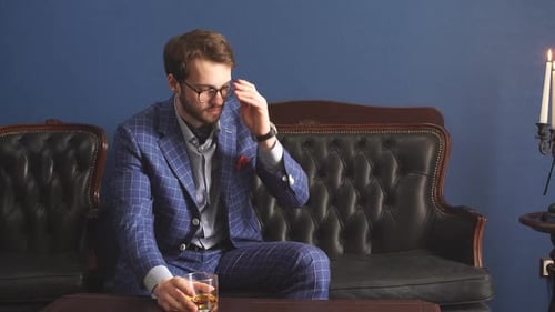 Handsome Young Man in a Classic Suit Drinking Whiskey in Restaurant