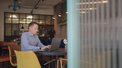 Man Works on Laptop in Modern Cafe Workspace