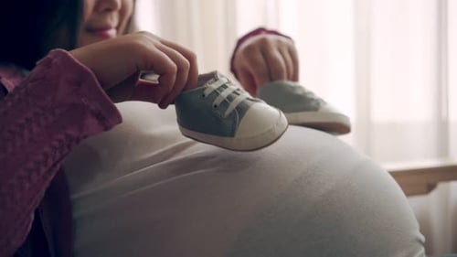 Pregnant Woman Holding Pair of Baby Shoes