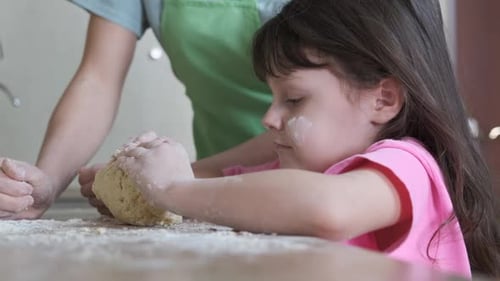 A child with his mother knead the dough.