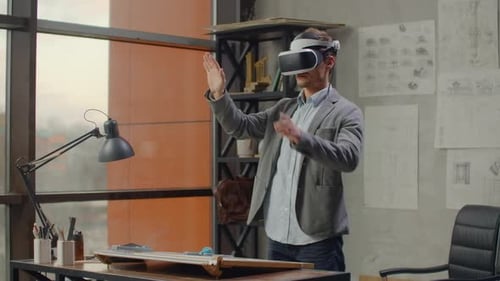 Modern Man Architect in the Office with Large Windows Stands in a Virtual Reality Helmet Uses