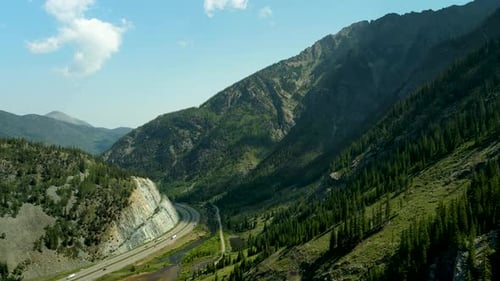 Volando por encima de una carretera muy abajo en el cañón debajo de los picos boscosos de las montañas